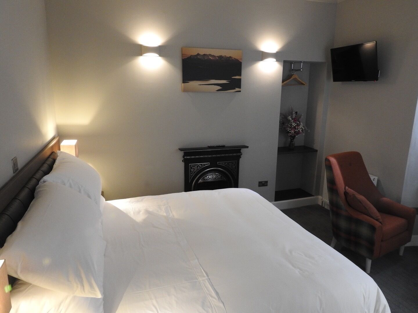 Een hotelkamer met een bed, een stoel, een open haard, een televisie en een wandlamp.