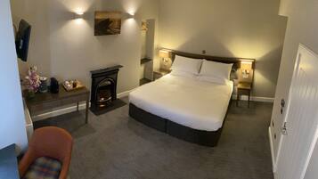 A neatly arranged hotel room with a bed, bedside tables, a small fireplace, and wall-mounted lighting.