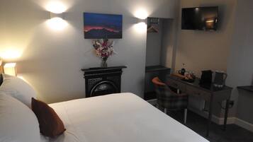 Quarto de hotel com cama, escrivaninha, cadeira, televisão e lareira.