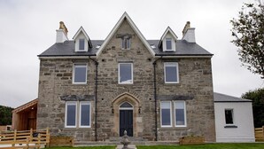 A stone building with a central entrance, multiple windows, and a small garden with a fountain. - House Of Juniper - The Manse (Strath)