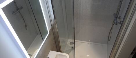 Un baño con ducha envuelta en vidrio, un lavabo y un espejo.