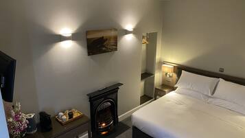 Una habitación de hotel con una cama, una chimenea, una mesita de noche, un espejo y una lámpara fijada a la pared.