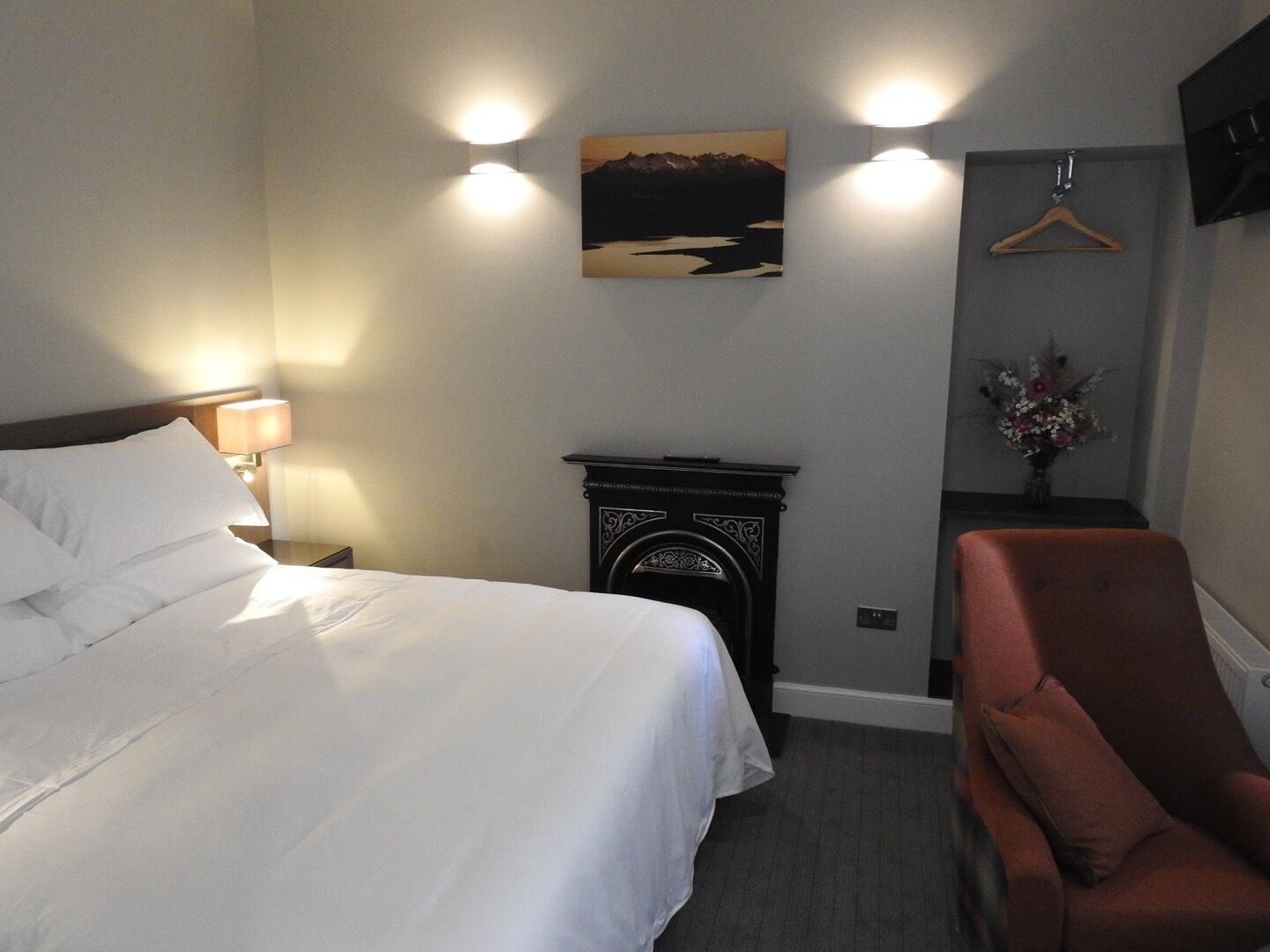 A hotel room with a bed, a chair, a fireplace, and a wall-mounted picture.
