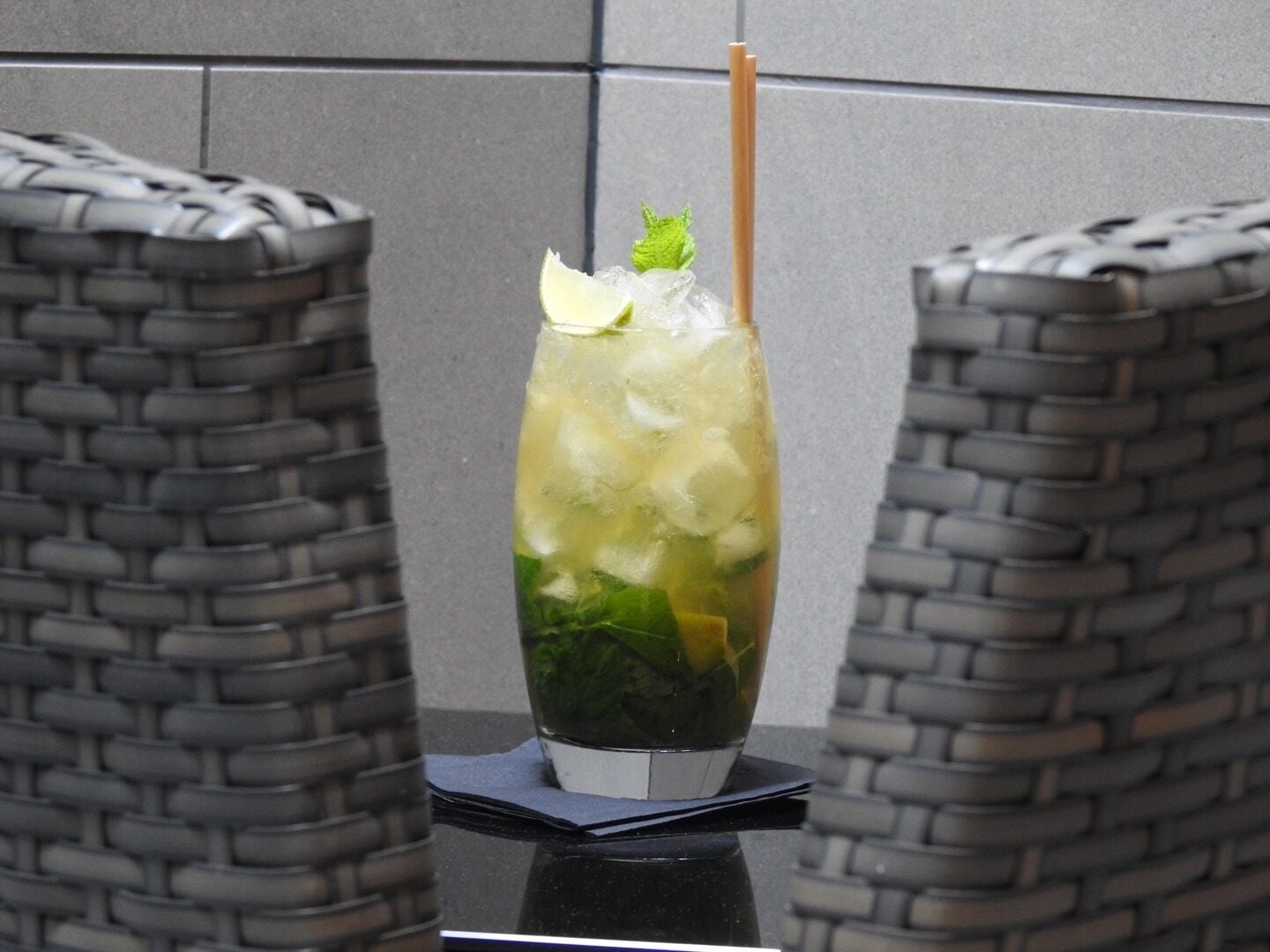 A drink in a glass with ice, lime, and mint on a reflective surface.