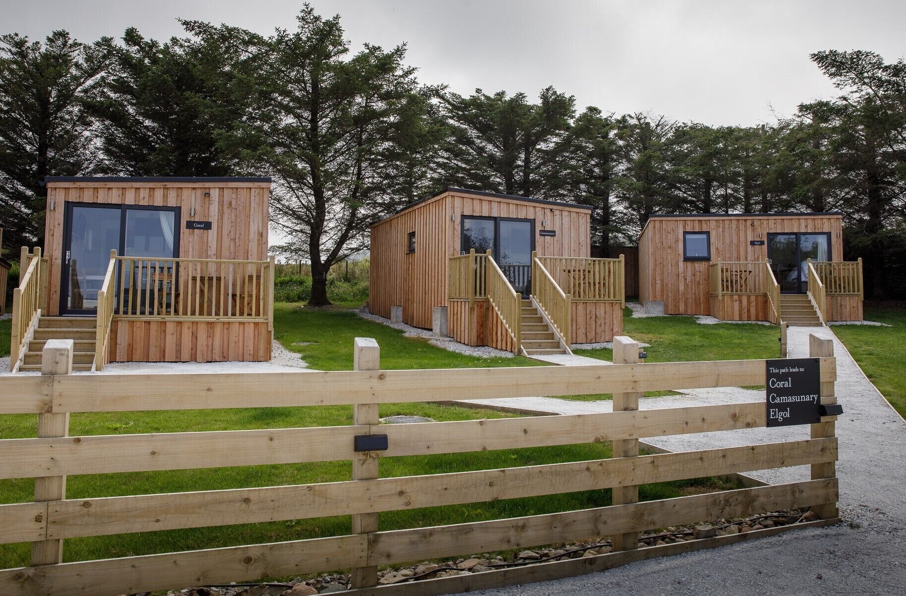Three wooden cabins with glass doors, each with a wooden deck and a staircase leading to the entrance.