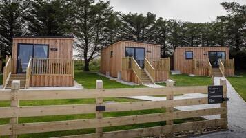 Three wooden cabins with glass doors, each with a wooden deck and a staircase leading to the entrance.