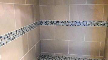 A shower room with tiled walls and floor, featuring a blue and gray mosaic border.
