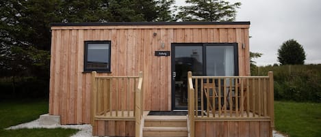 Una piccola baita di legno con una targa, una porta e una scala che conduce a un terrazzo.