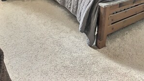 Un dormitorio con un cabecero de madera, una colcha acolchada gris y dos mesitas de noche con lámparas.