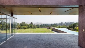 Een modern architecturaal interieur met een glazen gevel, een betonnen vloer en uitzicht op een aangelegde tuin met een zwembad.