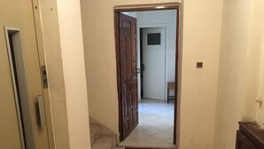 A narrow hallway with a wooden door at the end, a welcome mat, and a small table with a chair in the background.