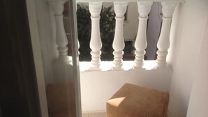 A balcony with white balustrades, a brown ottoman, and a view of a building in the background.