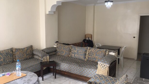 A living room with a sofa set, a dining table, and a small round table with a bottle and glasses.