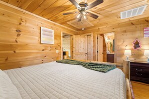 A wooden cabin bedroom with a bed, a ceiling fan, a wooden dresser, and a mirror.