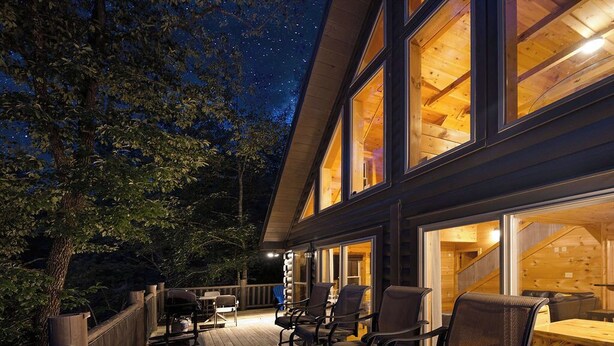 A wooden deck with outdoor seating and a large window overlooking the interior. - Smoky/ Mountain views/ King bed/ bunk bed/en suite bath/Hot tub/Sauna/Pet/value (Sevierville)