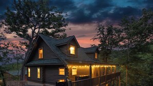 A log cabin with a deck and multiple windows, surrounded by trees. - Smoky/ Mountain views/ King bed/ bunk bed/en suite bath/Hot tub/Sauna/Pet/value (Sevierville)