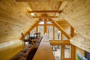 Un intérieur en bois avec une longue table et des chaises, de grandes fenêtres et une vue sur l’extérieur.