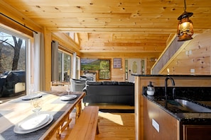 L’intérieur d’une cabane en bois comprend un coin repas, un canapé et une cuisine équipée d’un évier.