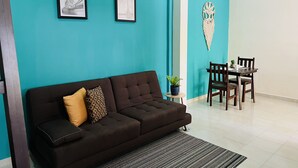 Una sala de estar con un sofá marrón oscuro, dos cuadros en la pared, una mesita con sillas y un adorno colgante.