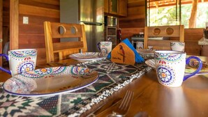 L’intérieur d’un chalet en bois présente une table à manger dressée avec de la vaisselle colorée, des chaises et un petit nichoir décoratif.