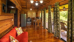 L’intérieur d’un chalet en bois comprend une cuisine, un coin repas et un canapé rouge agrémenté de coussins à motifs.