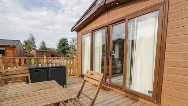 A wooden deck with a table and chairs, a sliding glass door, and a view of the surrounding area. - 22 Sherwood (Carnforth)