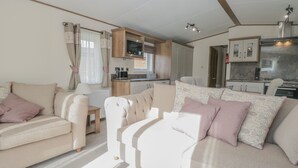 A compact living space with a sofa set, a small dining table, and a kitchenette area. - 22 Sherwood (Carnforth)