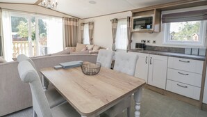A cozy living area with a sofa, a dining table, and a kitchen area with a microwave. - 22 Sherwood (Carnforth)