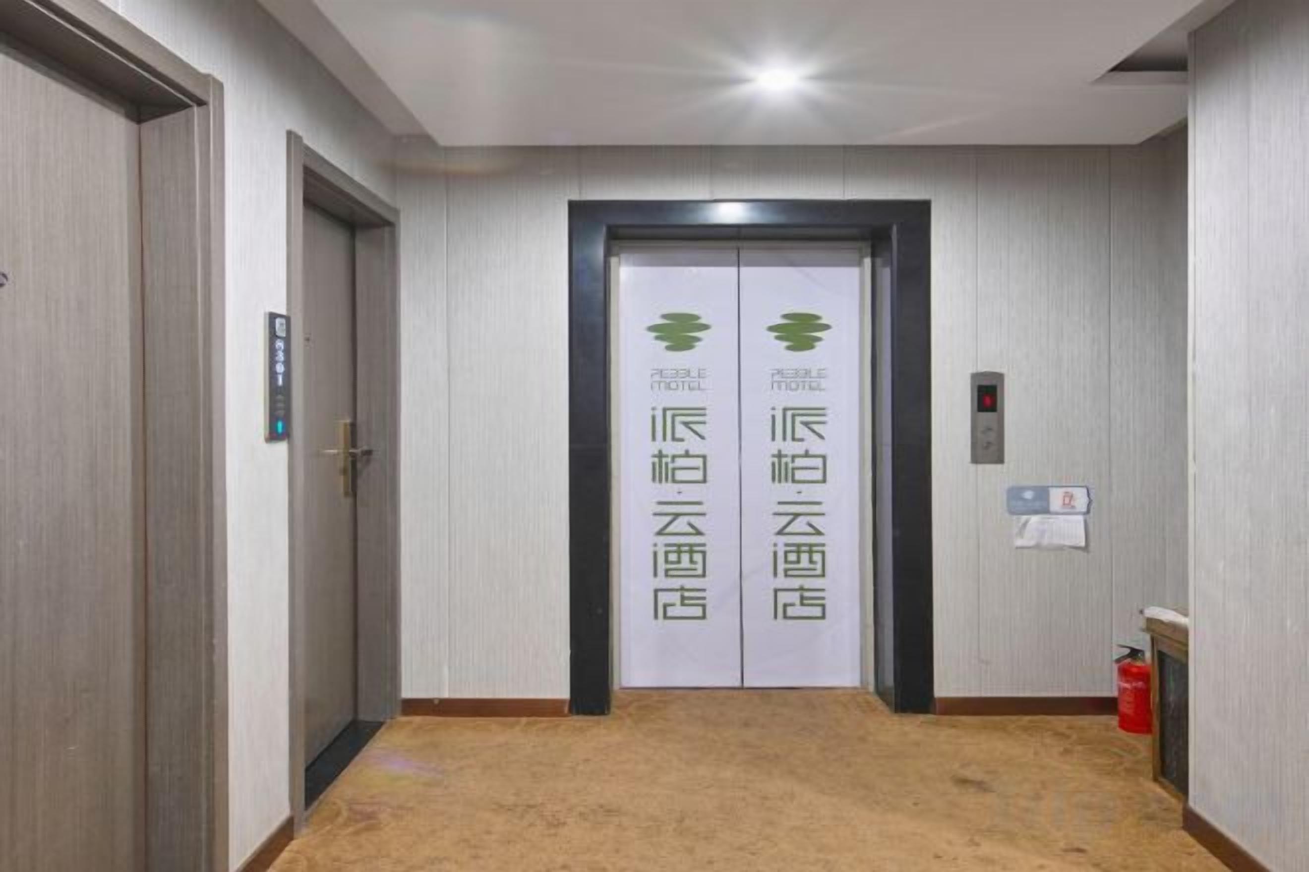 A hotel corridor with two doors, each marked with a green logo and Chinese characters, and a fire extinguisher on the right wall.