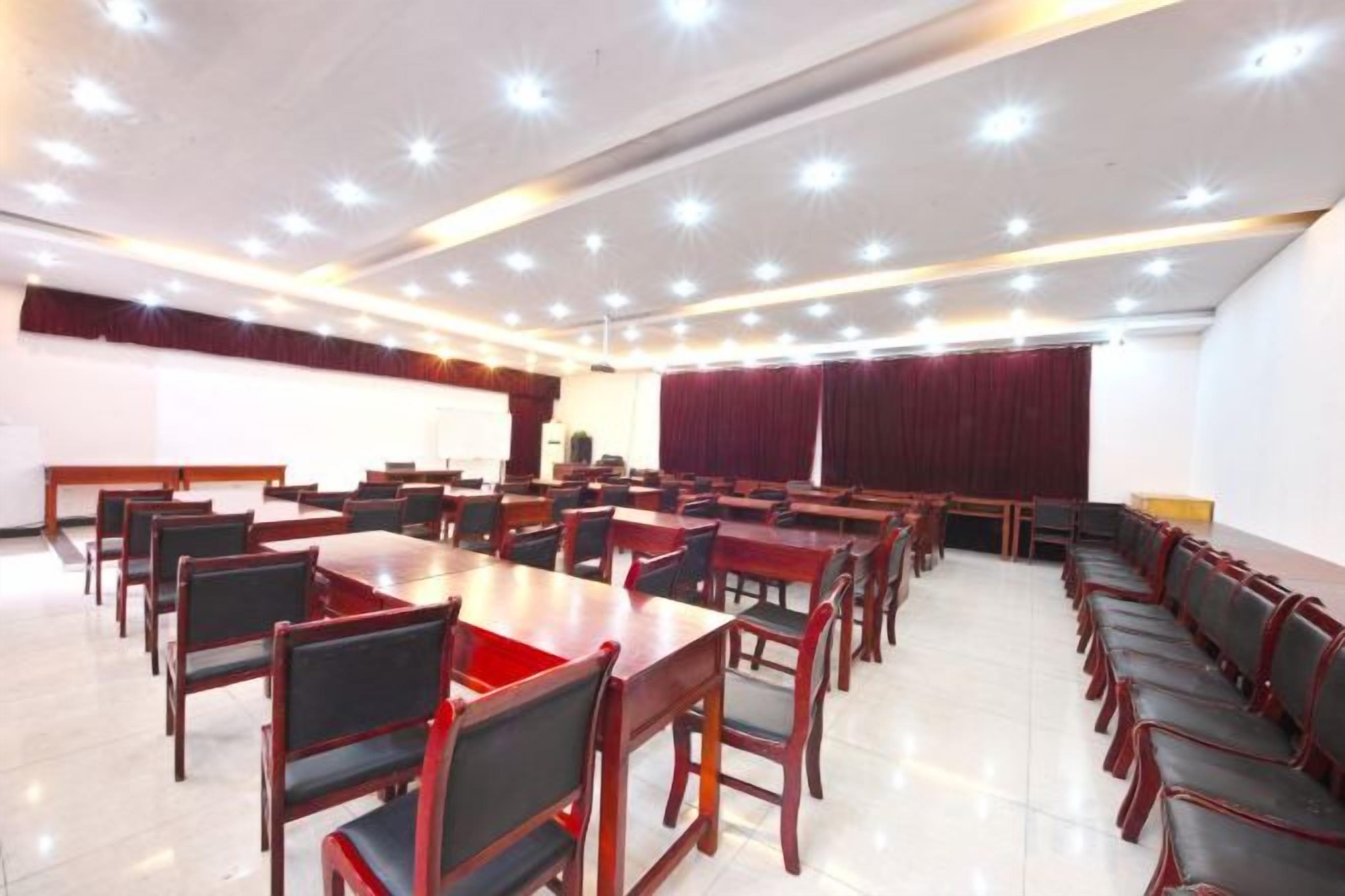 Un salón de conferencias con varias mesas y sillas, un escenario con un atril y una cortina roja grande.