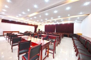 Un salón de conferencias con varias mesas y sillas, un escenario con un atril y una cortina roja grande.