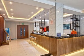 A hotel reception area with a wooden counter, bar stools, a reception desk, and a digital display. - Pebble Motel Cloud Hotel (Chaohu Wanda Plaza) (Chaohu)