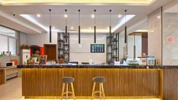 Una cocina moderna con una isla central, taburetes de bar, iluminación colgante y una pantalla digital con el menú.