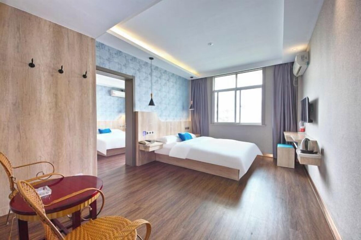 A modern hotel room with a wooden floor, a bed with white bedding, a red chair, a small table, and a TV on the wall.