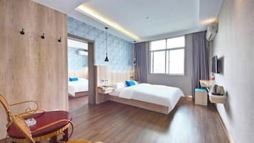A modern hotel room with a wooden floor, a bed with white bedding, a red chair, a small table, and a TV on the wall.