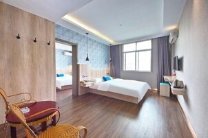 Una habitación de hotel moderna con suelo de madera, cama con ropa blanca, una silla roja, una mesita pequeña y un televisor en la pared.