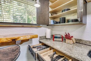 Une cuisine dotée d’un plan de travail en bois, d’un four encastré et d’une fenêtre avec des stores.