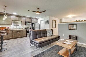 A modern kitchen with stainless steel appliances, a dining area with a leather sofa, and a ceiling fan.