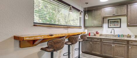 A kitchen with wooden cabinets, a bar area with stools, and a window with blinds.