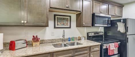 A kitchen with wooden cabinets, a stainless steel sink, a microwave, a stove, and a toaster.