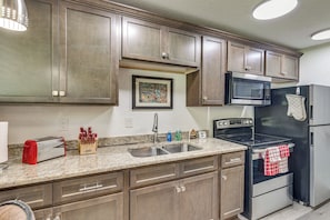 A kitchen with wooden cabinets, a stainless steel sink, a microwave, a stove, and a toaster.