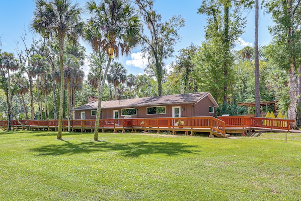 A cabin with a deck, surrounded by tall trees and a grassy area.