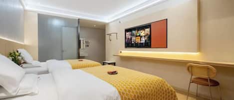 A hotel room with two beds, a TV mounted on the wall, and a small desk with a chair.