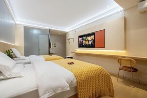 Quarto de hotel com duas camas, uma televisão presa à parede e uma pequena escrivaninha com uma cadeira.