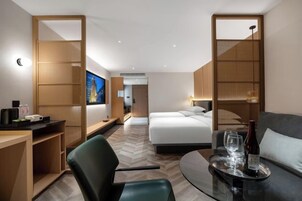 Quarto de hotel com cama, escrivaninha, poltrona, sofá e mesa de jantar.