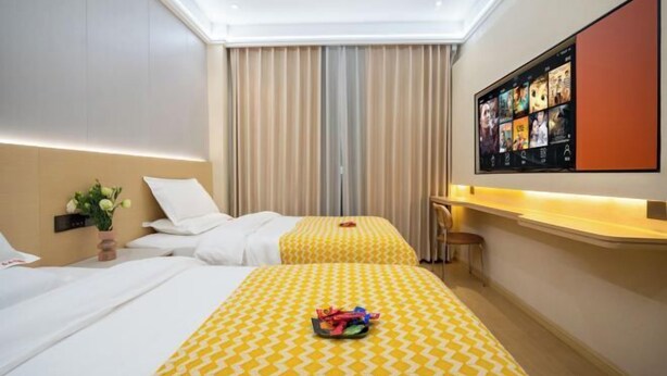 Habitación de hotel con dos camas, un ventanal grande con cortinas, un televisor de pantalla plana en la pared y una mesita con una silla.