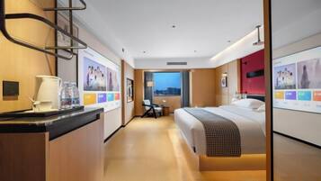 A hotel room with a bed, a desk, a chair, a window with a view, and a wall with framed pictures.