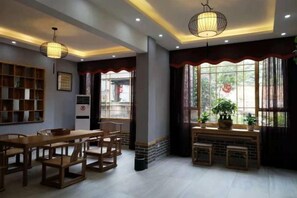 A dining area with wooden furniture, a bookshelf, and a window with curtains. - Banshan Bieyuan Inn (Yanjin)