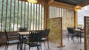 A covered outdoor seating area with tables and chairs, large windows, and a wooden ceiling. - Banshan Bieyuan Inn (Yanjin)