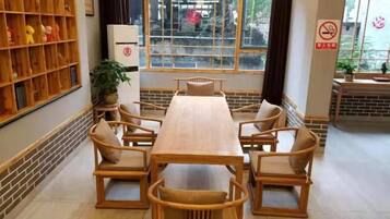 A dining area with a long wooden table and chairs, a bookshelf, and a window with a view.